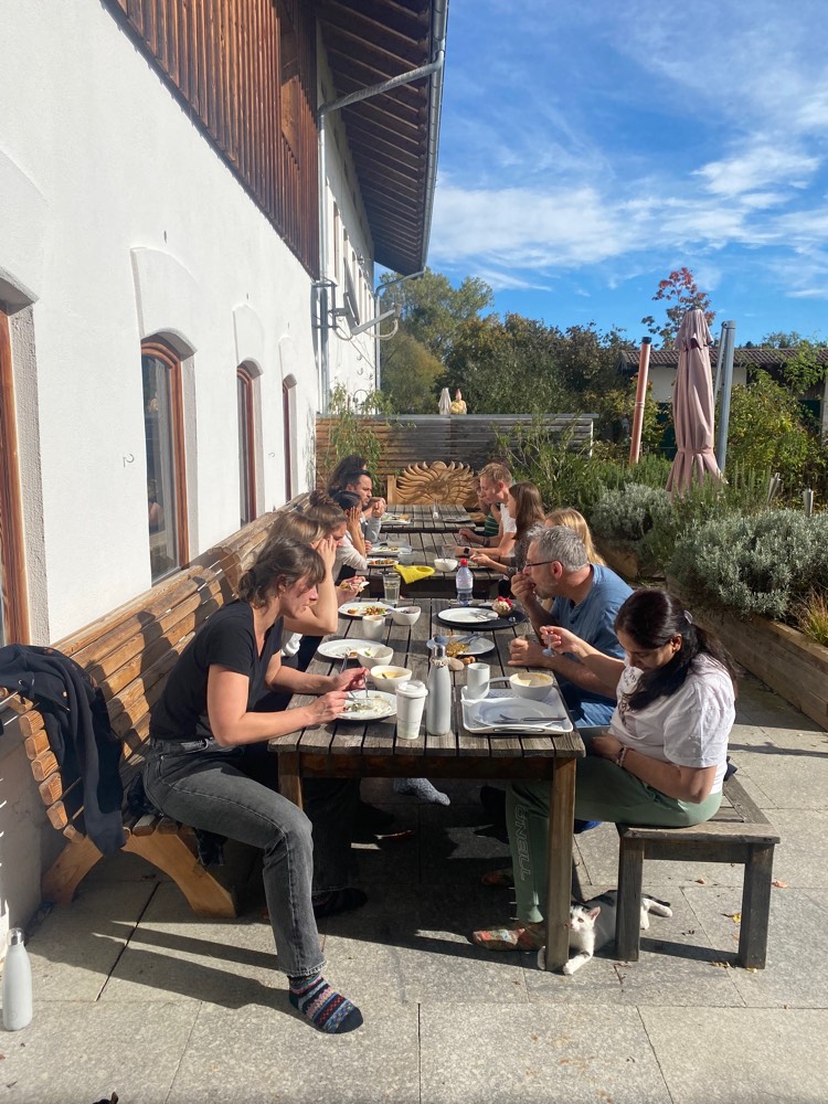 Gäste beim gemeinsamen Essen an einer langen Tafel in der Sonne vor der Hütte
