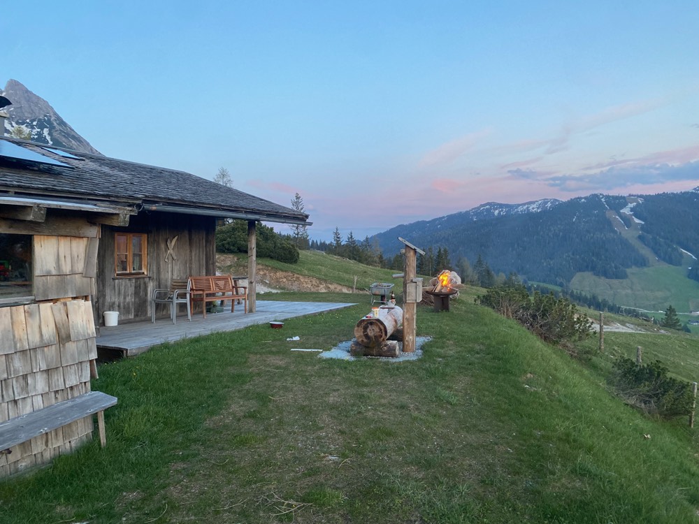 Abendlicht über der Alm, Gäste ruhen auf der Wiese neben der Hütte